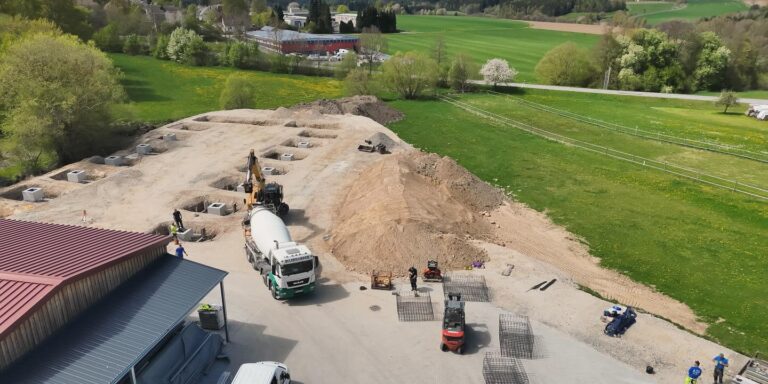 Drohnenaufnahme einer Baustelle mit Aushubarbeiten, Fundamentgruben und Baufahrzeugen zur Vorbereitung eines Neubaus.