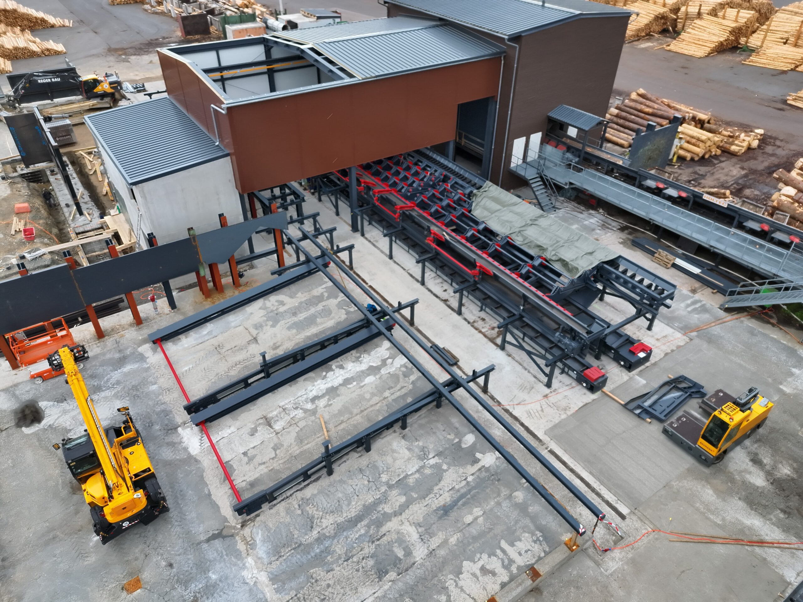 Drohnenaufnahme einer industriellen Holzbearbeitungsanlage während der Bau- oder Erweiterungsphase. Fördertechnik, Maschinenanlagen und Stahlkonstruktionen sind aus der Vogelperspektive zu sehen und verdeutlichen die technische Komplexität des Projekts.