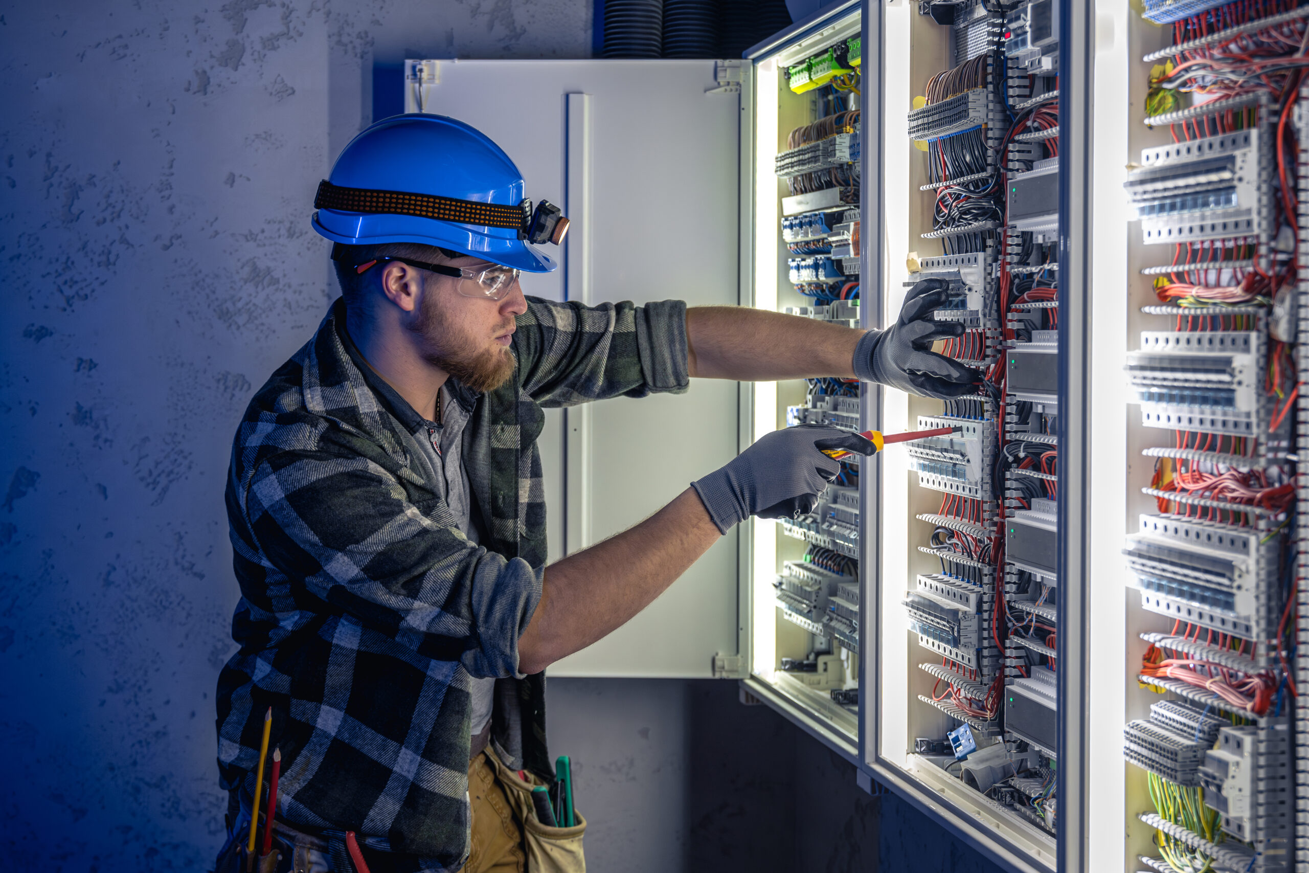 Schaltschrankbau und professionelle Elektroinstallation Elektriker arbeitet an einem geöffneten Schaltschrank und prüft die Verdrahtung einer elektrischen Anlage.