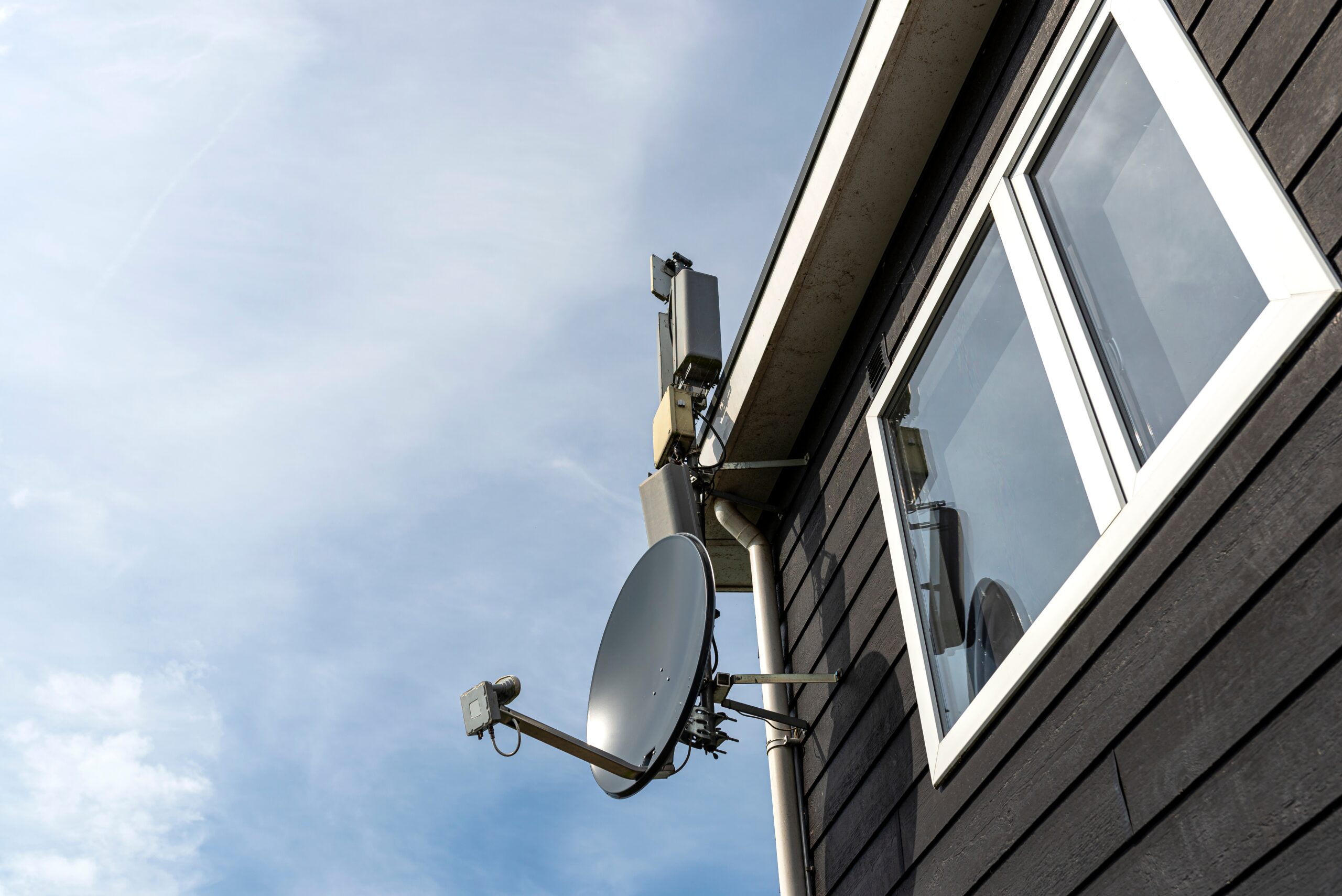 Satellitenanlage für zuverlässige Kommunikation Satellitenschüssel und Kommunikationstechnik an der Außenfassade eines Gebäudes für Empfangs- und Telekommunikationslösungen.