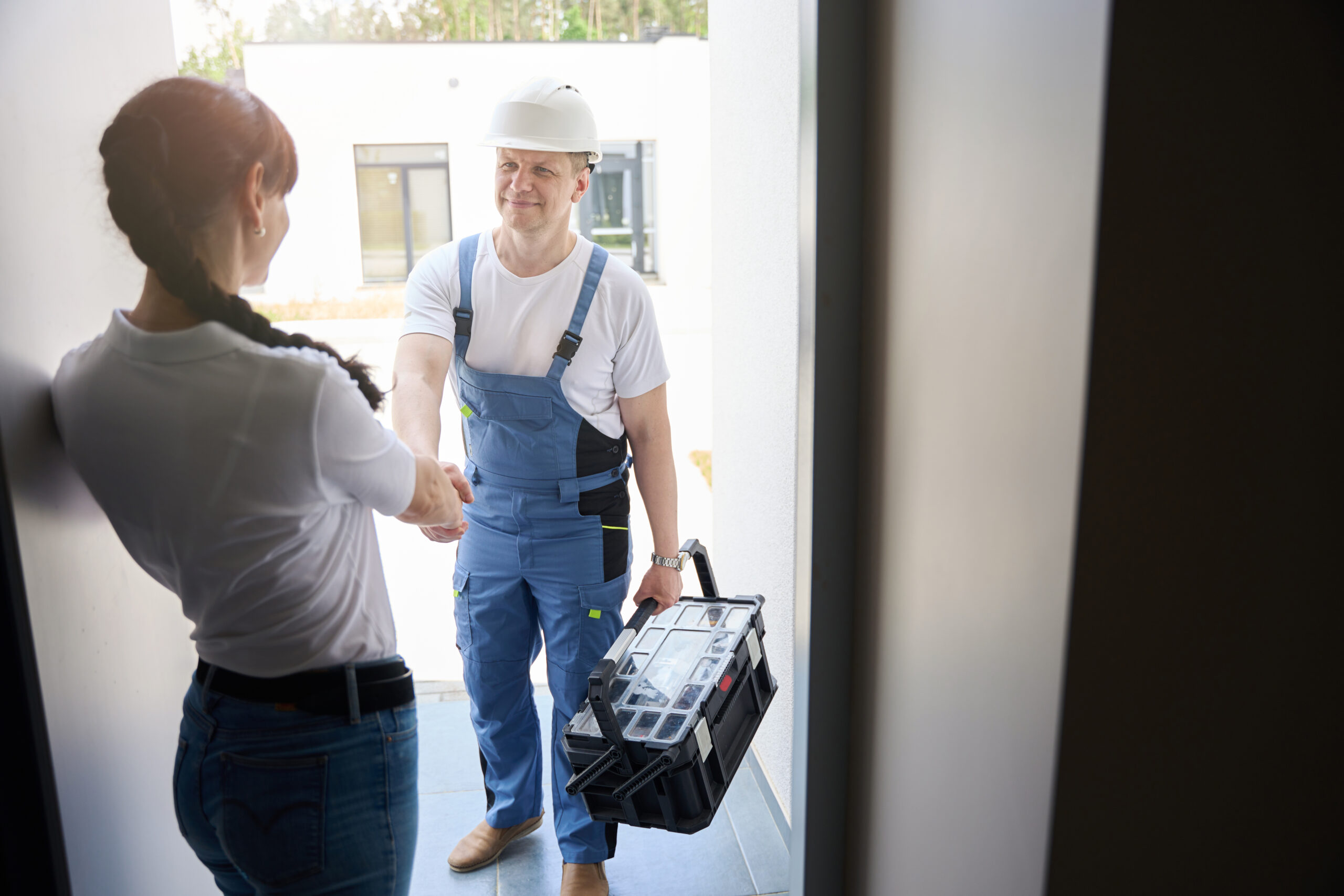 Zuverlässiger Service vor Ort Servicetechniker begrüßt eine Kundin an der Haustür und ist für einen Vor-Ort-Termin mit Werkzeugkoffer angekommen.